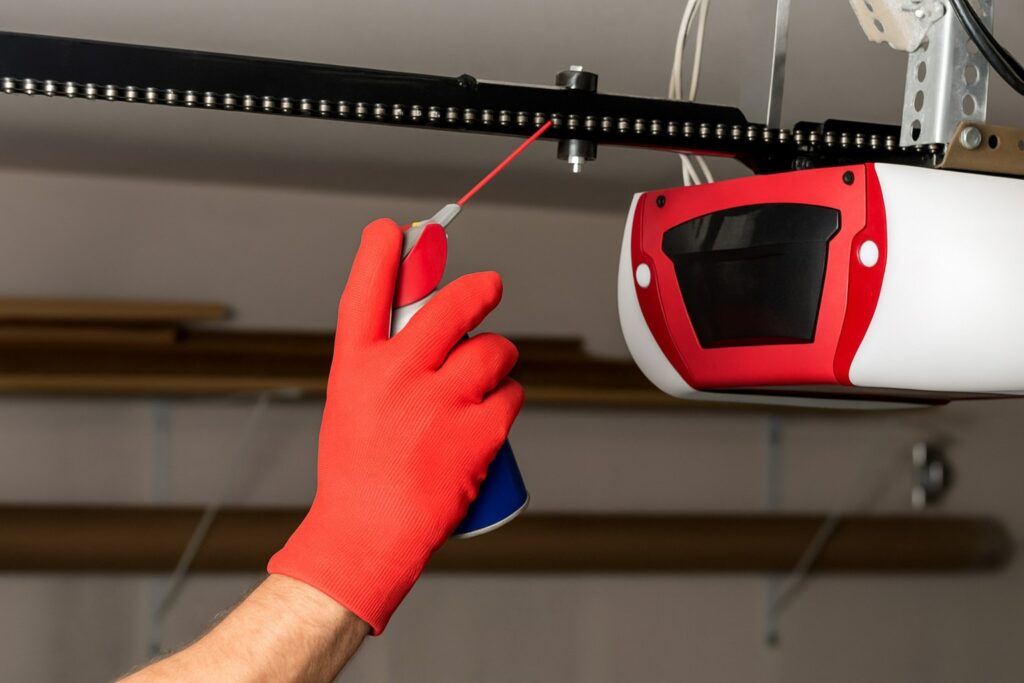 Technician lubricating chain mechanism during garage door opener repair for smooth operation.